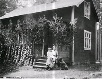 Kvinna med barn och hund framför ett hus
