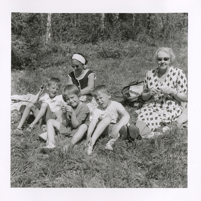 Brita och barnen sitter på en filt i gröngräset med svärmor, 1950-tal.