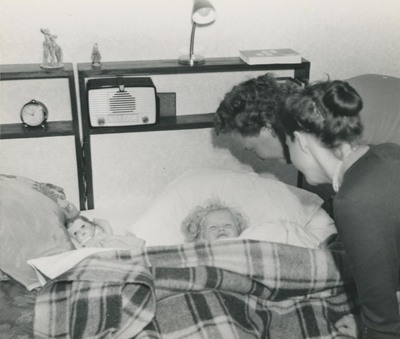 Ett barn i en säng, två kvinnor står bredvid