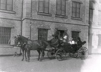 En häst och vagn med tre kvinnor utanför en byggnad.