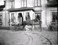 Man med häst och vagn framför byggnad