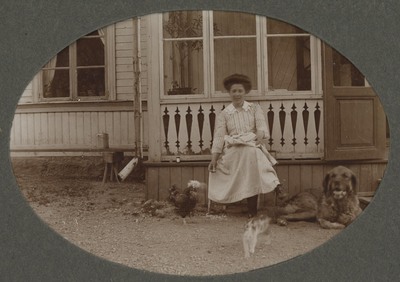 Kvinna framför hus med hund, katt och höna