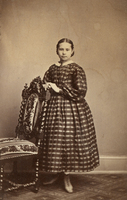 Ung flicka vid stol, klädd i vid klänning, 1860-tal