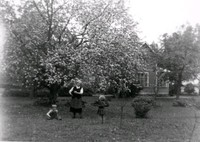 En sköterska och två barn i en trädgård.