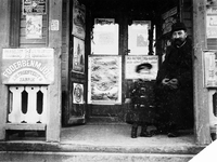 Man och barn framför en butik med olika reklamaffischer, 1897