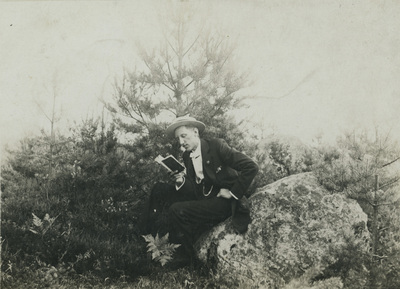 En man sitter på en sten och läser en bok